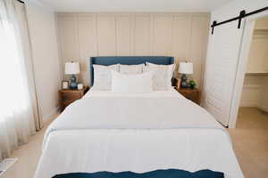 Bedroom featuring a barn door, a decorative wall, light carpet, visible vents, and a walk in closet