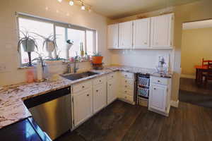 Kitchen featuring dark wood-type flooring, dishwasher, a sink, and light stone countertops