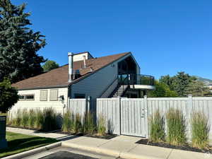 View of side of property with roof with shingles, a chimney, a gate, fence, and stairs