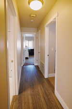 Corridor with dark wood-style floors, visible vents, and baseboards