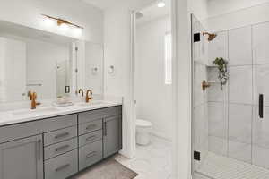 Bathroom with a stall shower, a sink, toilet, and double vanity