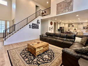 Living area with baseboards, recessed lighting, stairs, light wood-style floors, and a towering ceiling