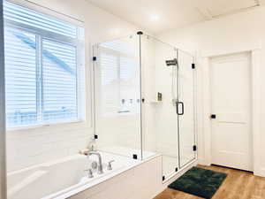 Bathroom with wood finished floors, a healthy amount of sunlight, a stall shower, and a bath