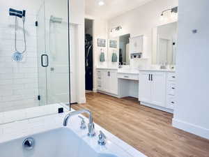 Bathroom with a shower stall, baseboards, wood finished floors, a bath, and vanity