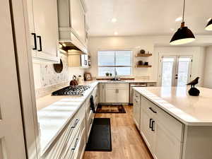 Kitchen with light wood finished floors, open shelves, decorative backsplash, appliances with stainless steel finishes, and a sink