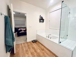 Bathroom with baseboards, tiled shower, wood finished floors, and a bath