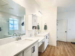 Bathroom featuring a shower stall, baseboards, two vanities, wood finished floors, and a sink