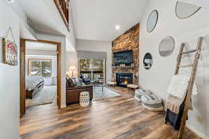 Living area featuring high vaulted ceiling, baseboards, wood finished floors, and a stone fireplace