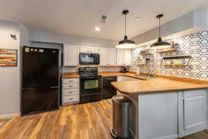 Kitchen with light wood-style flooring, white cabinetry, a sink, a peninsula, and black appliances