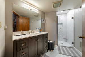 Full bath with a textured ceiling, vanity, a shower stall, and visible vents