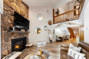 Living area with high vaulted ceiling, a stone fireplace, wood finished floors, baseboards, and stairway