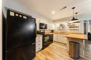 Kitchen featuring light wood finished floors, visible vents, black appliances, white cabinetry, and a sink