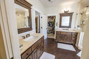 Full bath with wood-type flooring, two vanities, visible vents, a sink, and a shower stall