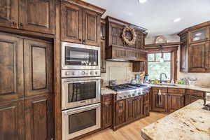 Kitchen with light stone countertops, stainless steel appliances, a sink, decorative backsplash, and light wood finished floors