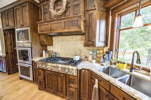 Kitchen with light wood finished floors, stainless steel appliances, tasteful backsplash, a sink, and light stone countertops