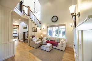 Living area featuring light wood-type flooring, a notable chandelier, a decorative wall, and stairs