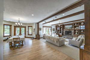 Living room with a textured ceiling, beamed ceiling, a brick fireplace, and light wood-style flooring