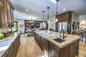 Kitchen with decorative light fixtures, dark brown cabinetry, a sink, light wood-type flooring, and high end refrigerator