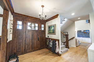 Entryway with light wood-style flooring, wooden walls, stairway, and a chandelier