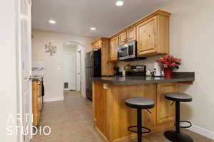 Kitchen with arched walkways, stainless steel appliances, dark countertops, recessed lighting, and a kitchen bar