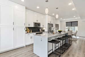 Kitchen with stainless steel appliances, a breakfast bar, white cabinetry, light wood finished floors, and a center island with sink