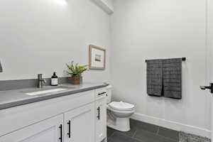 Half bath featuring toilet, tile patterned flooring, baseboards, and vanity