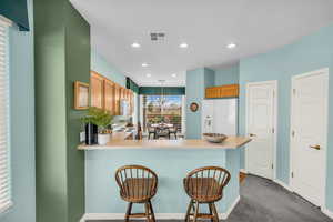 Kitchen featuring visible vents, dark carpet, white fridge with ice dispenser, a peninsula, and a kitchen breakfast bar