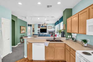 Kitchen featuring visible vents, a sink, a warm lit fireplace, white appliances, and a peninsula