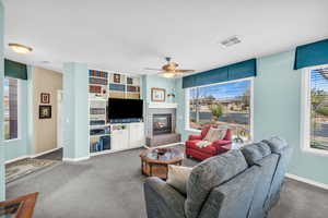 Carpeted living room with a ceiling fan, visible vents, a fireplace, and baseboards