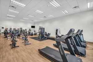 Gym with a paneled ceiling, wood finished floors, and visible vents