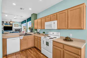 Kitchen featuring white appliances, visible vents, a lit fireplace, light wood-style floors, and a sink