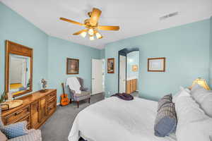 Carpeted bedroom with arched walkways, visible vents, ceiling fan, and ensuite bathroom