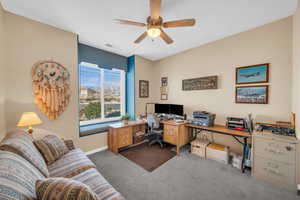 Carpeted home office with baseboards, visible vents, and a ceiling fan