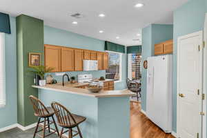 Kitchen with a peninsula, white appliances, visible vents, a kitchen breakfast bar, and light countertops