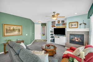 Carpeted living area with a ceiling fan, a tile fireplace, built in features, and baseboards