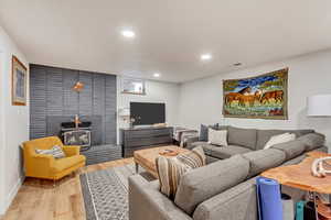 Living room featuring light wood finished floors, recessed lighting, visible vents, a wood stove, and baseboards