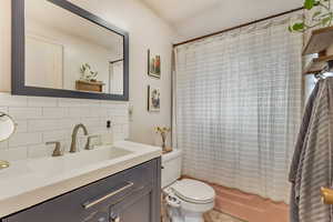 Full bath featuring toilet, tasteful backsplash, shower / tub combo with curtain, and vanity