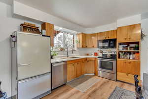 Kitchen with light wood-style flooring, a sink, light countertops, appliances with stainless steel finishes, and tasteful backsplash