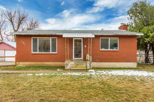 Bungalow with brick siding, an outdoor structure, fence, a chimney, and a front yard