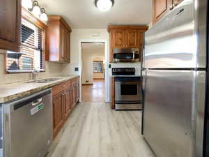 Kitchen featuring arched walkways, light wood finished floors, backsplash, appliances with stainless steel finishes, and a sink