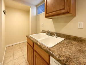 Kitchen featuring baseboards, brown cabinetry, dark countertops, a sink, and light tile patterned flooring