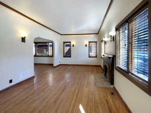 Unfurnished living room with arched walkways, visible vents, a brick fireplace, wood finished floors, and baseboards