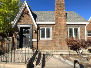 View of front facade with a shingled roof, brick siding, and a chimney