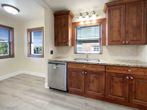 Kitchen featuring light stone counters, backsplash, stainless steel dishwasher, and healthy amount of natural light