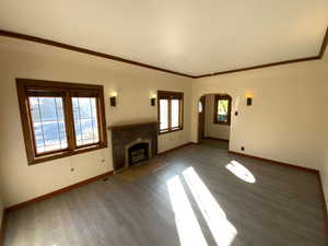 Unfurnished living room with arched walkways, a fireplace with flush hearth, ornamental molding, and wood finished floors
