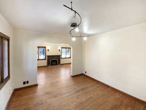 Unfurnished room with light wood-style flooring, arched walkways, baseboards, and a fireplace with flush hearth