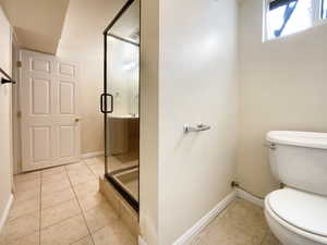 Bathroom with toilet, tile patterned flooring, baseboards, and a shower stall