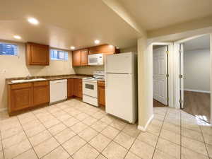 Kitchen with white appliances, brown cabinets, light tile patterned floors, recessed lighting, and dark countertops