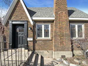 View of exterior entry with a shingled roof, a chimney, and brick siding