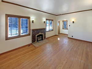 Unfurnished living room with light wood finished floors, visible vents, baseboards, a tile fireplace, and crown molding